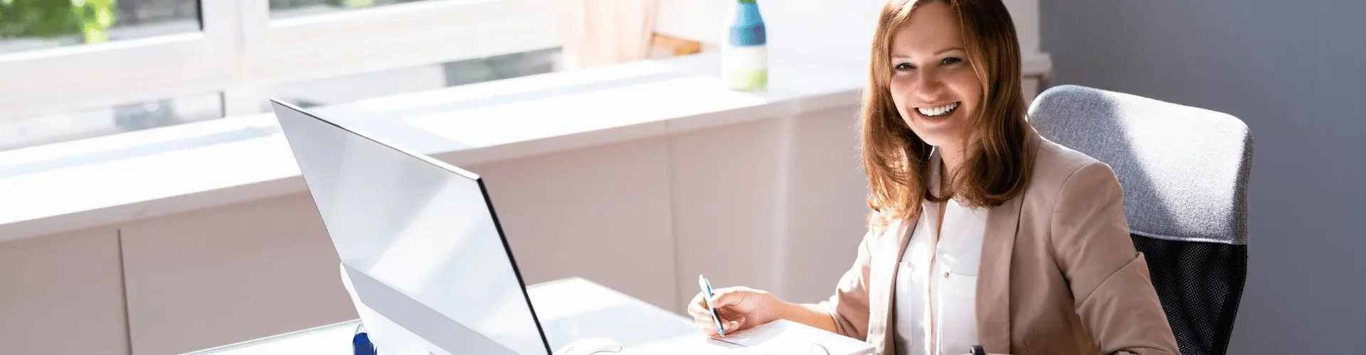 Junge Bankkauffrau arbeitet mit Computer, Ordner und Taschenrechner