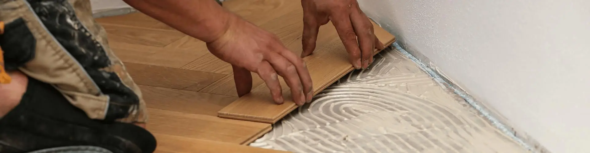 Bodenleger reiht Stücke eines neuen Parkettbodens aneinander