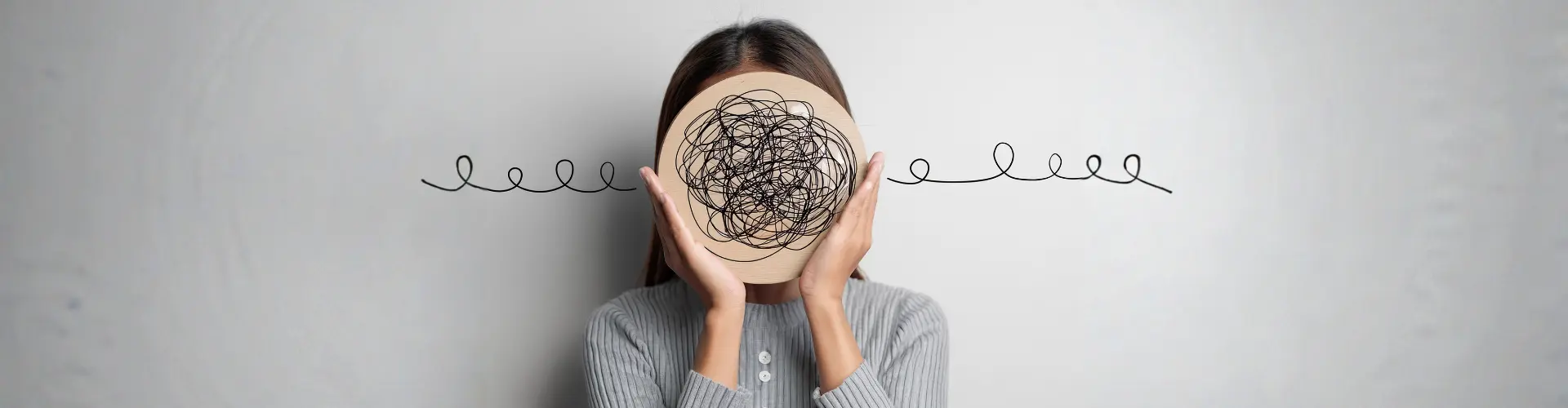 Frau hält eine Holzscheibe mit verworrenen schwarzen Linien vor das Gesicht, Linien führen nach außen. Symbolisiert innere Unruhe oder Gedankenchaos.