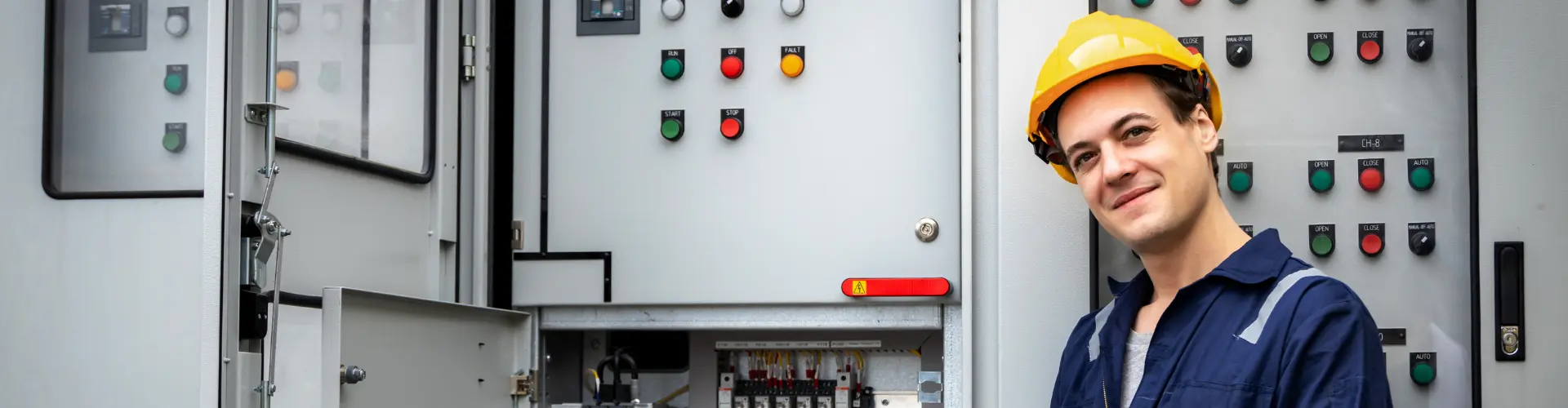 Student im dualen Studium Elektrotechnik steht mit Schutzhelm vor einem Schaltschrank