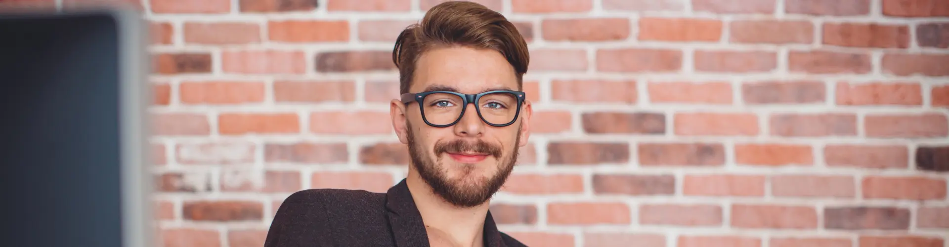 Student im dualen Studium Kommunikationsdesign arbeitet am Laptop vor einer Backsteinwand