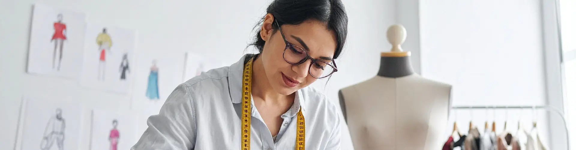 Studentin im dualen Studium Modedesign arbeitet im Atelier mit Maßband und Modeentwürfen