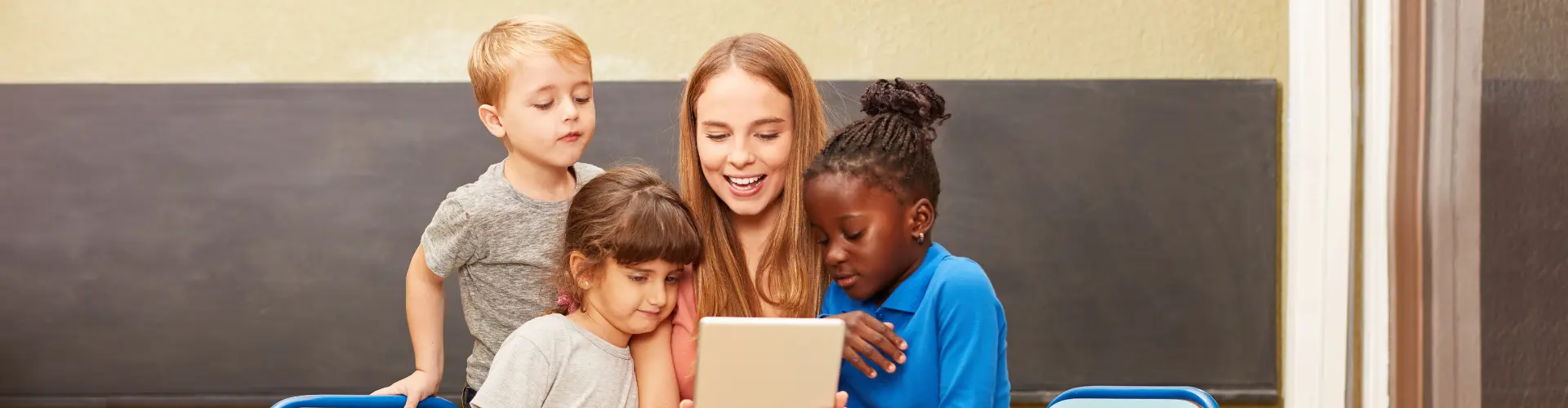 Studentin im dualen Studium Sozialpädagogik sitzt mit mehreren Kindern und hält ein Tablet