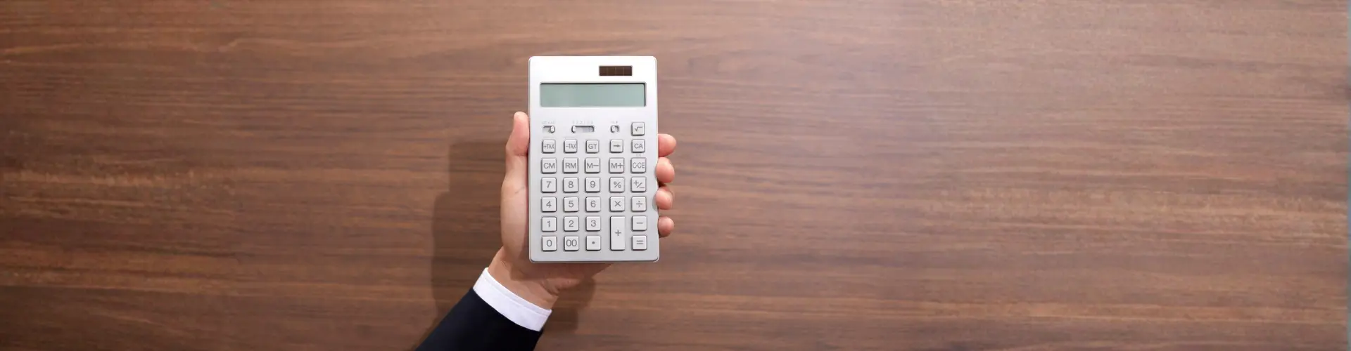 Das Bild zeigt eine Hand mit Taschenrechner vor Holz-Hintergrund – es steht für Steuern und Abgaben in der Ausbildung.