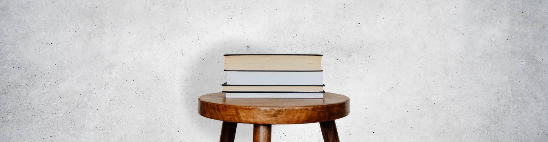 Das Bild zeigt einen Holzstuhl, auf dem mehrere Bücher gestapelt sind – es steht für Wissen, Bildung oder Lernen.