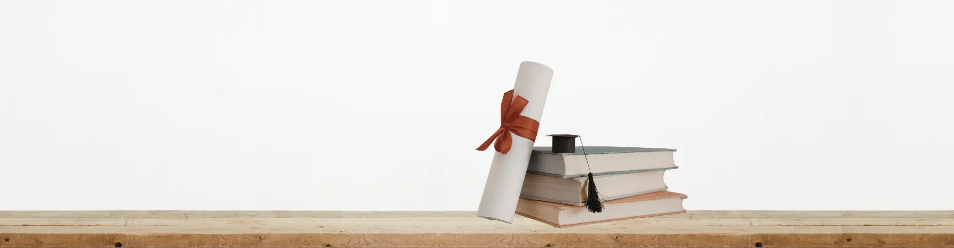 Das Bild zeigt Bücher, eine Abschlussrolle mit Schleife und einen kleinen Doktorhut – es steht für Bildung, Abschluss oder akademischen Erfolg.