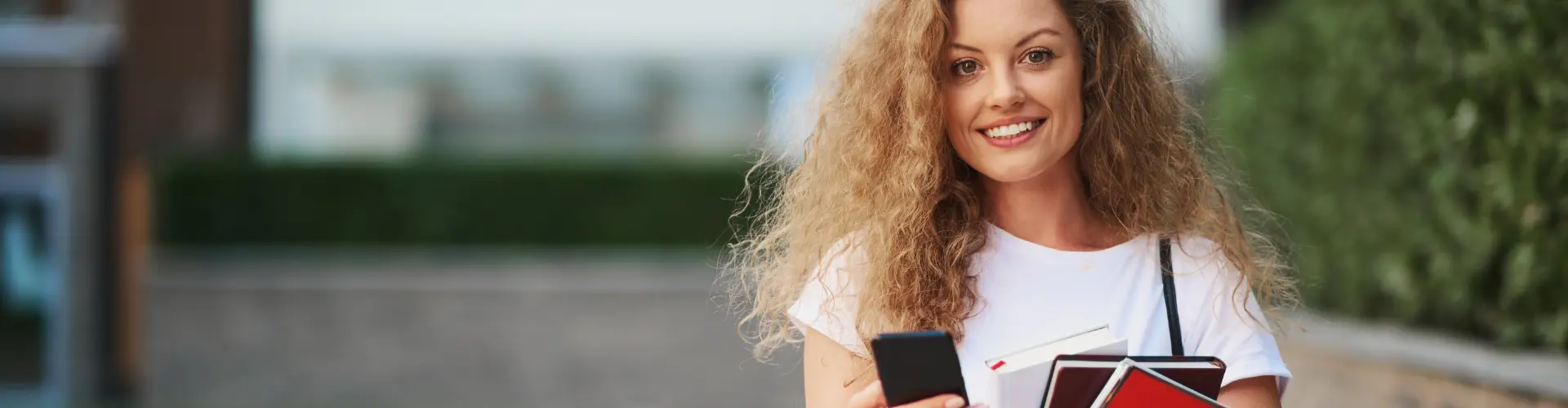 Junge Frau mit Handy und Büchern in der Hand