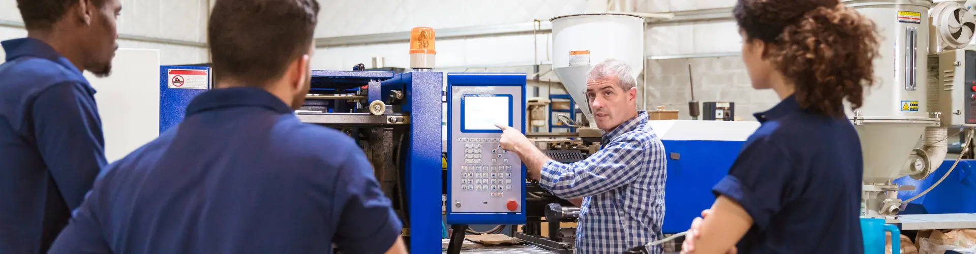 Mann zeigt 3 Azubis etwas an einer Maschine