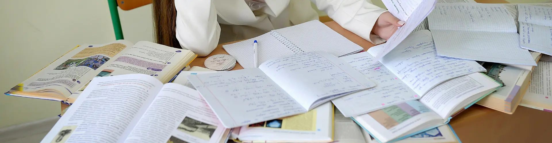 Frau sitzt an einen Schreibtisch und lernt auf dem Tisch liegen viele Hefte und Bücher