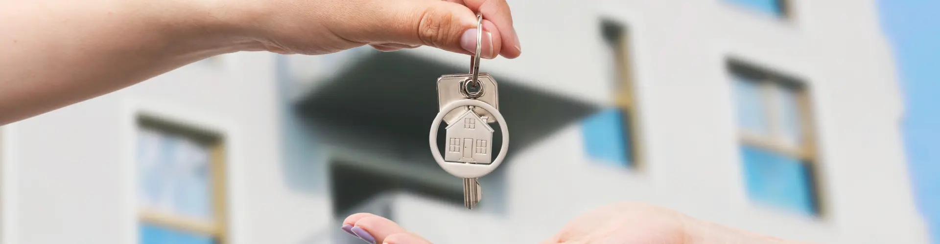 ein Schlüssel wird übergeben und im Hintergrund ist ein Wohnhaus
