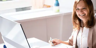 Junge Bankkauffrau arbeitet mit Computer, Ordner und Taschenrechner