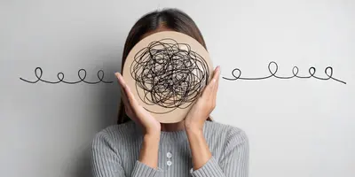 Frau hält eine Holzscheibe mit verworrenen schwarzen Linien vor das Gesicht, Linien führen nach außen. Symbolisiert innere Unruhe oder Gedankenchaos.