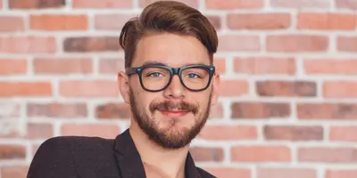 Student im dualen Studium Kommunikationsdesign arbeitet am Laptop vor einer Backsteinwand