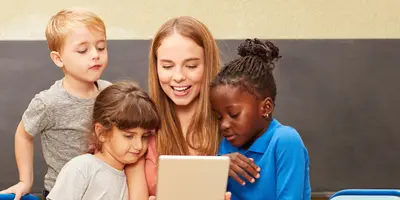 Studentin im dualen Studium Sozialpädagogik sitzt mit mehreren Kindern und hält ein Tablet