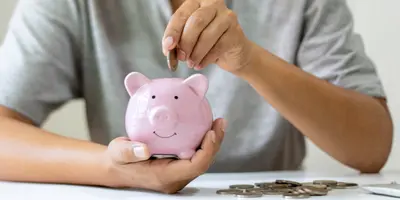 Das Bild zeigt eine Person, die Münzen in ein Sparschwein steckt – es steht für BAföG und finanzielle Unterstützung während der Ausbildung oder des Studiums.