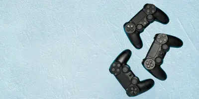 Das Bild zeigt drei schwarze Spiel-Controller auf hellblauem Hintergrund – es steht für Gaming oder gemeinsames Spielen.