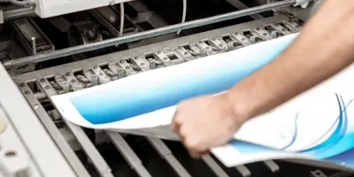 Medientechnologe steht an Druckmaschine und betrachtet Papier