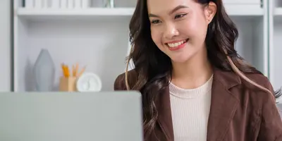 junge Frau sitzt lächelnd vor Laptop