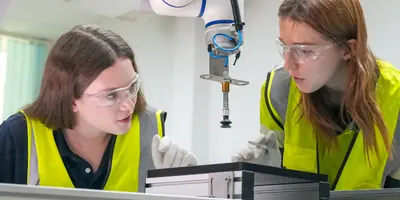 zwei junge Mädchen in Warnwesten hinter einer Maschine