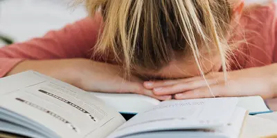 junges Mädchen mit Kopf auf dem Tisch und Bücher auf dem Tisch