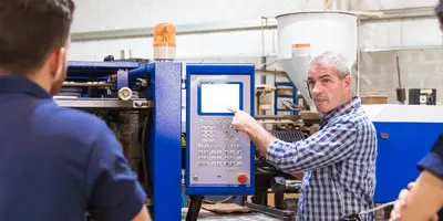 Mann zeigt 3 Azubis etwas an einer Maschine