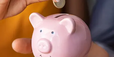 eine Frau hält ein Sparschwein in der Hand und wirft eine Münze rein