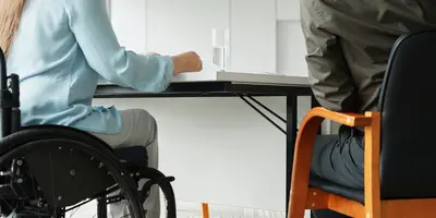 4 Personen davon eine Person im Rollstuhl sitzen an einem Tisch