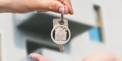 ein Schlüssel wird übergeben und im Hintergrund ist ein Wohnhaus