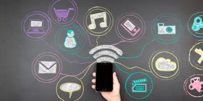 eine Hand mit Smartphone vor einer Wand mit bunten Symbolen – es steht für Social Media, digitale Vernetzung und Kommunikation